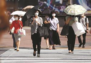 マスクをつけ日傘を差して歩く人たちの写真