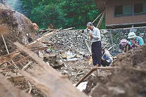 土砂崩れの犠牲になった人の自宅跡で手を合わせる人たちの写真
